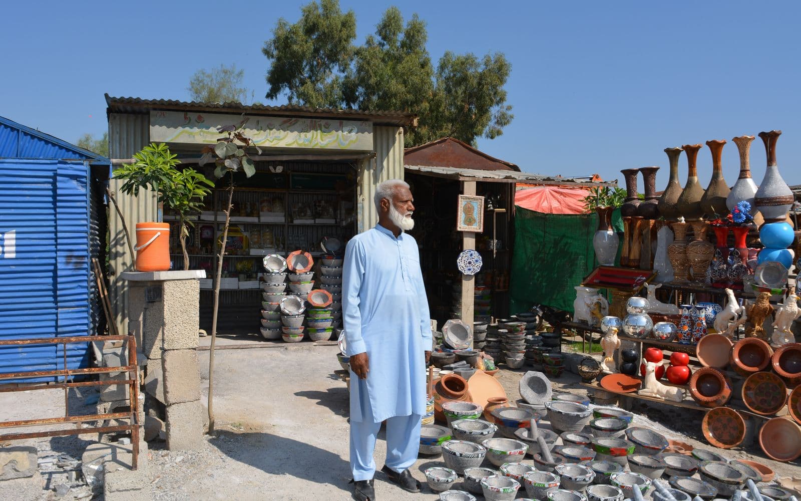 Pakistani artisan standing outside his pottery and handicraft shop