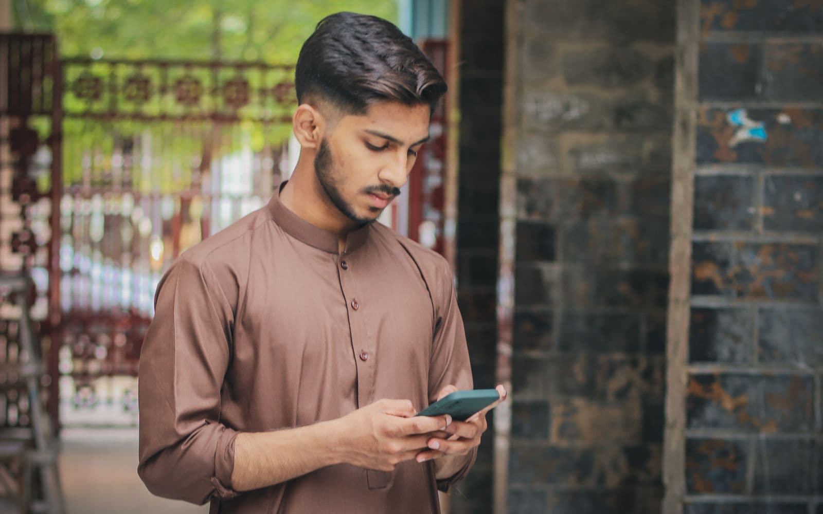 Young Pakistani man in shalwar kameez using an app on his smartphone