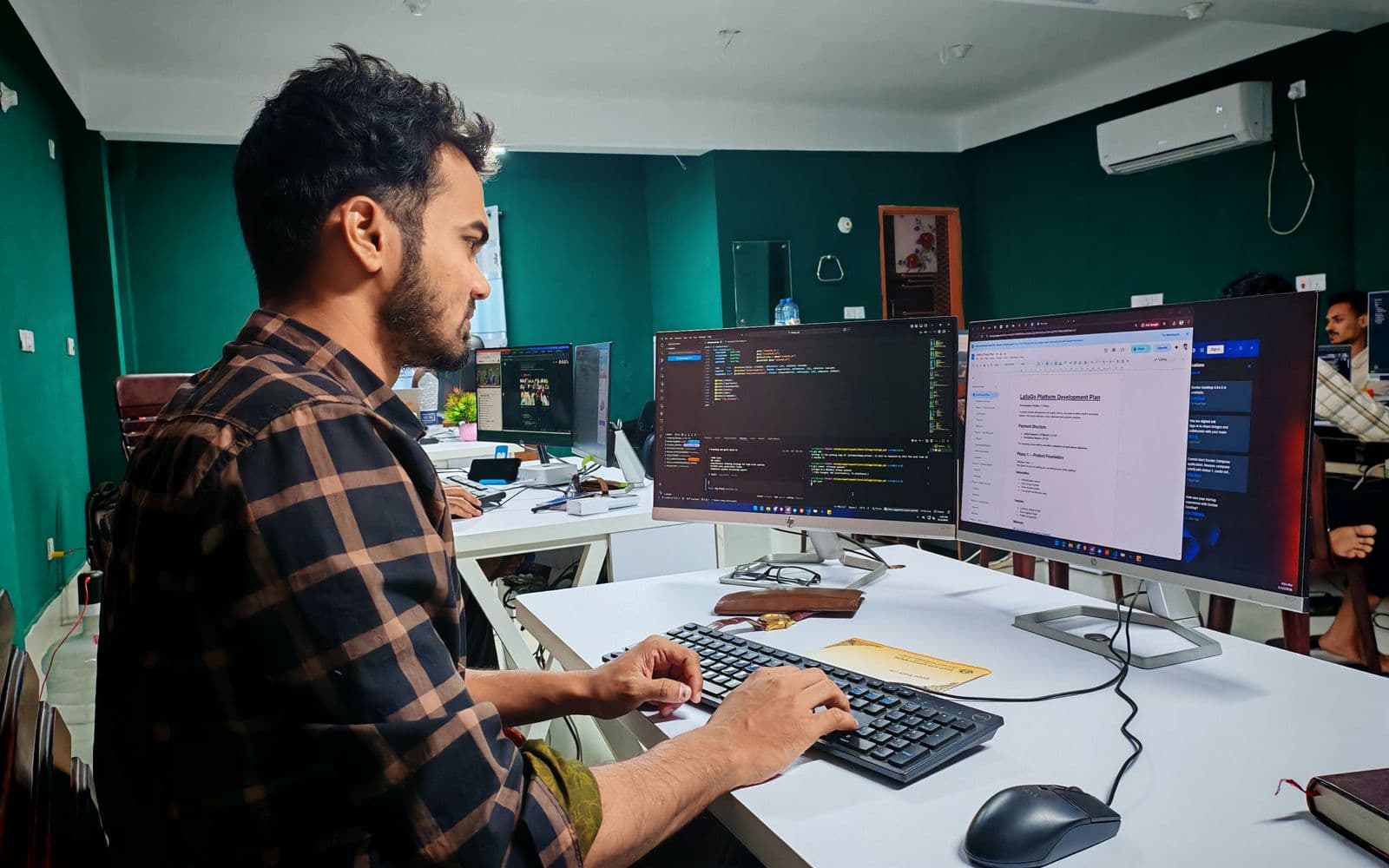 Software developer writing code on dual monitors in a modern office