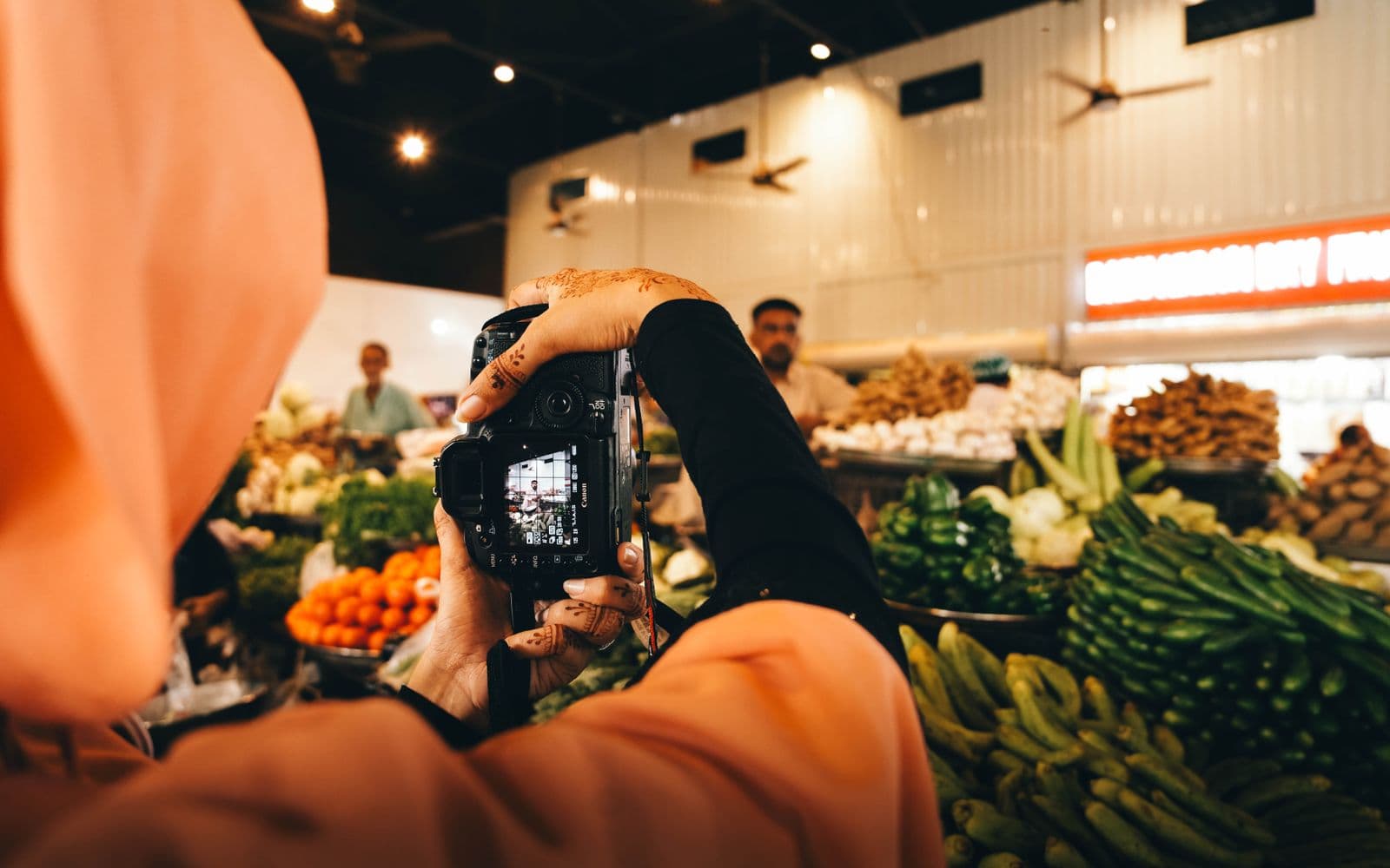 Woman with henna-decorated hands photographing fresh vegetables at a market in Sindh for social media
