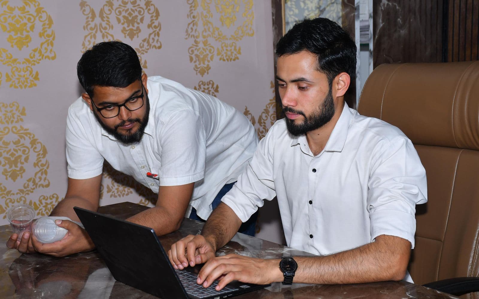 Two Pakistani web developers reviewing a website project on a laptop